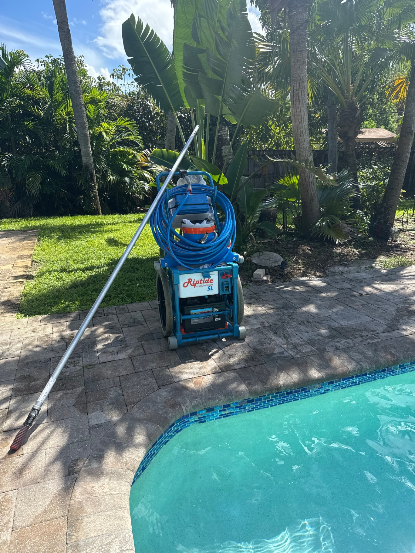 Riptide SL pool vacuum system and pole staged on a paver deck next to a Palm Beach pool