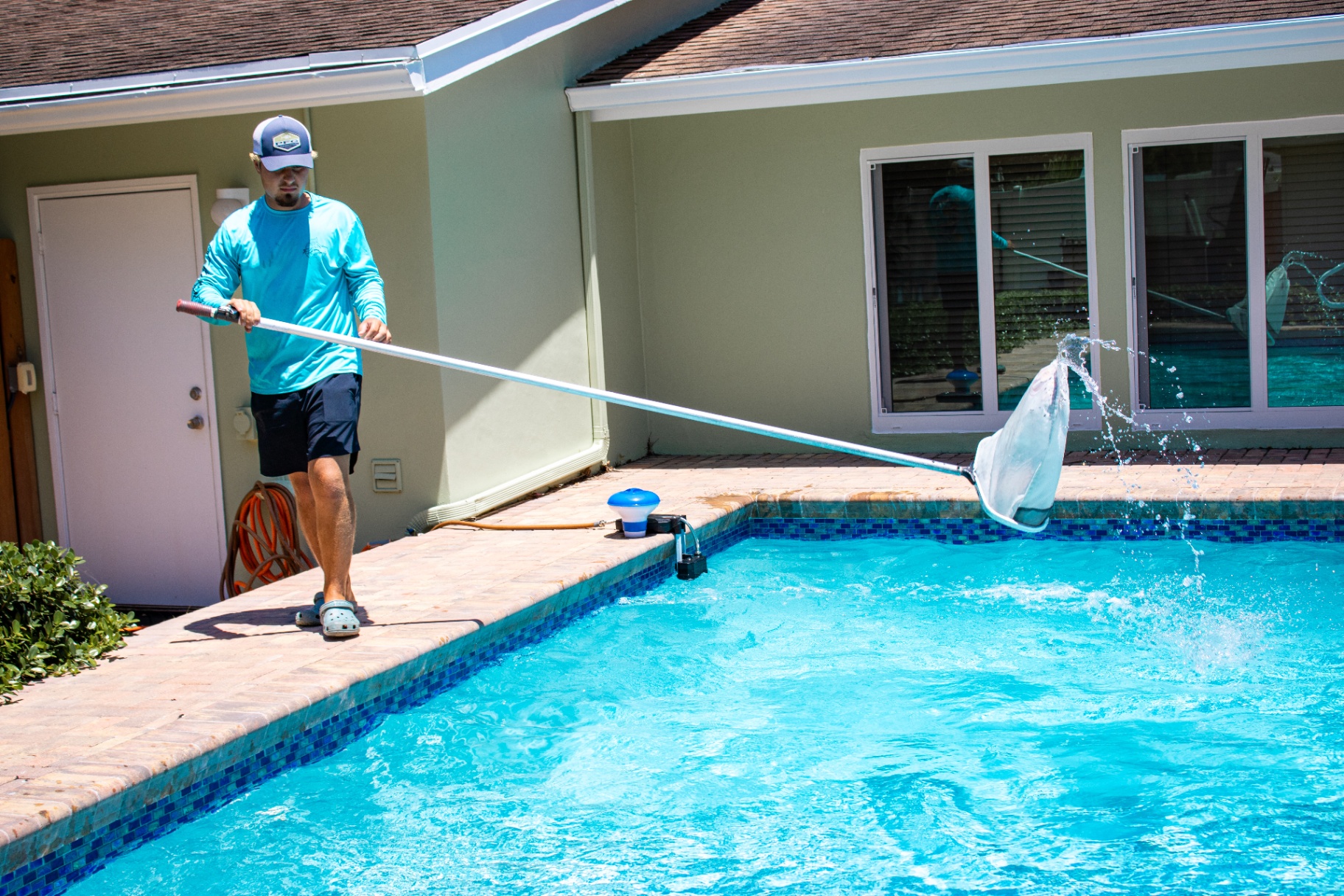Collegiate Pools technician skimming leaves from a backyard pool in Palm Beach County, FL